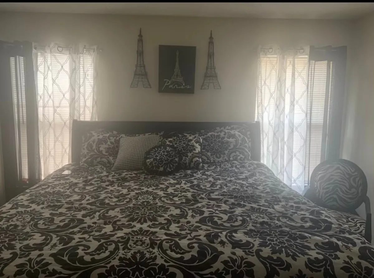 The image showcases a bright, inviting bedroom with a bed adorned in patterned bedding, striking Eiffel Tower wall art above the headboard, and a bold zebra-patterned accent chair. Sunlight pours through the window, creating a cozy and stylish atmosphere that encourages relaxation and quiet moments.