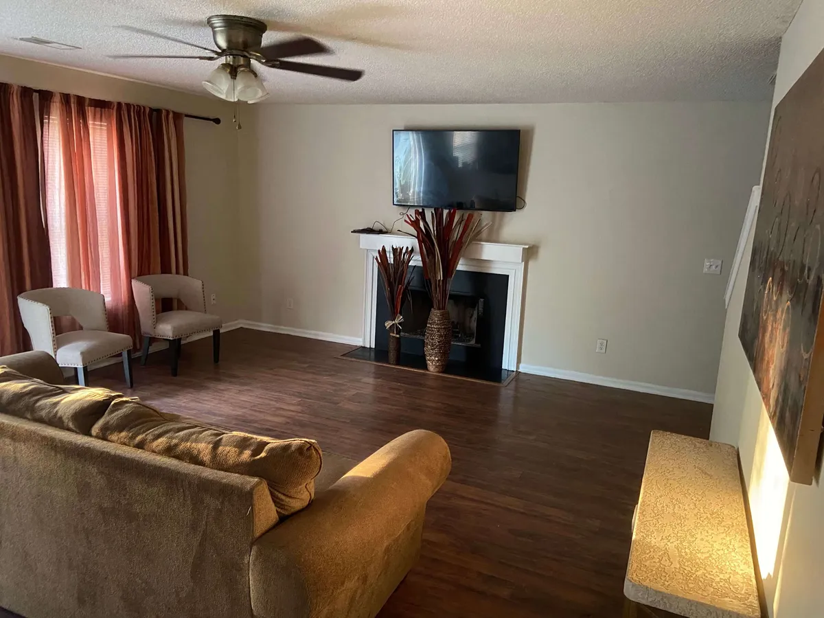 A comfortable living room with a plush sofa, fireplace, TV, and cozy chairs arranged to encourage gatherings. Soft curtains diffuse the light, and the setting is ideal for relaxing or socializing after a long day.