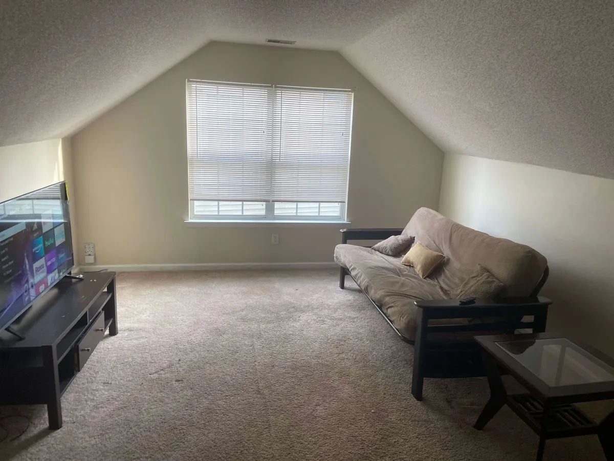 A casual living space with a TV, sofa, and large window, arranged for easy relaxation and entertainment. The natural light and layout highlight comfort and accessibility.