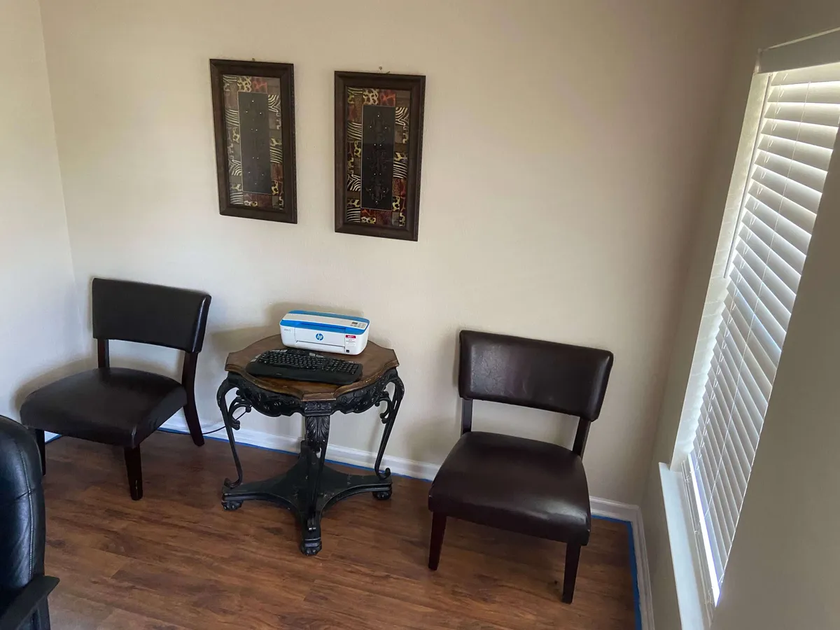 The image features a cozy interior setting with two chairs positioned around an ornate table, complemented by framed artwork on the walls. The inviting mood, decorative details, and arrangement suggest a communal atmosphere ideal for casual conversations or shared moments.